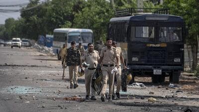 Broken glass and debris strewn on a street as policemen patrol after communal clashes in Nuh, on Tuesday. (AP)