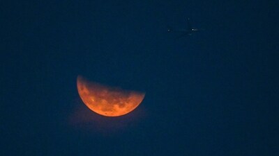 A passenger aircraft flies past a Sturgeon moon rising as seen from Singapore on Tuesday. (AFP)