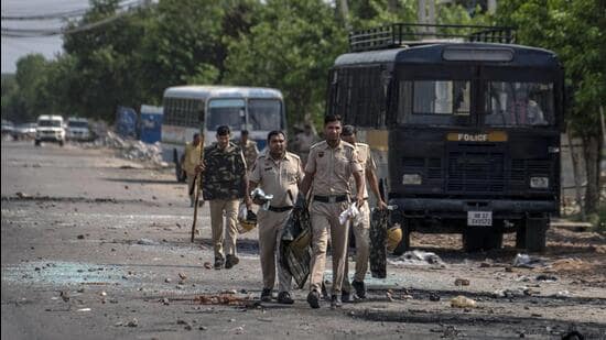 Broken glass and debris strewn on a street as policemen patrol after communal clashes in Nuh, on Tuesday. (AP)