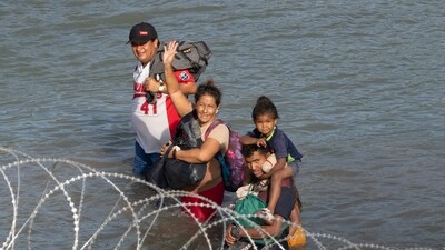 Migrants wave as they walk near concertina wire in the water along the Rio Grande border with Mexico in Eagle Pass, Texas, on July 16. (AFP) Migrants wave as they walk near concertina wire in the water along the Rio Grande border with Mexico in Eagle Pass, Texas, on July 16. (AFP)
