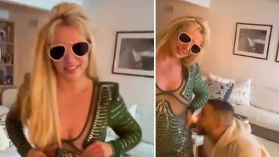 A man is seen in the video licking Britney Spears' leg as she stands ina room wearing a green mini dress and knee-high white boots (britneyspears/Instagram) A man is seen in the video licking Britney Spears' leg as she stands ina room wearing a green mini dress and knee-high white boots (britneyspears/Instagram)