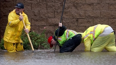 Workers attempt to unclog a drain on a flooded street as Tropical Storm Hilary moves through the area in Rancho Mirage, California.&nbsp; (AFP)
