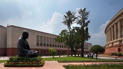 A statue of Mahatma Gandhi sits between the old and new Parliament House buildings on the opening day of the monsoon session of the Indian parliament, in New Delhi, India. (AP)