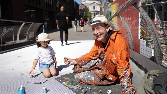 Ben Wilson, artist, shows Naiara, 4, how to hold a paintbrush, while he paints on the Millennium Bridge, London, Britain, August 21, 2023. (REUTERS/Anna Gordon)