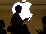 A women uses an iPhone mobile device as she passes a lighted Apple logo at the Apple store