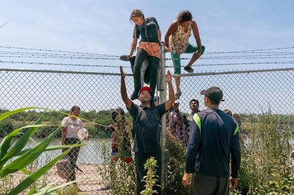 TOPSHOT - Migrants help each other climb over a barbed wire fence into the US from Mexico, in Eagle Pass, Texas, on August 25, 2023. With their two children on their shoulders, Wilfredo and Nataly jump into the Rio Grande from the Mexican shore. The water is up to their waists. They avoid the line of buoys that the state of Texas placed to block their passage and head for the United States. They cross from Piedras Negras, Coahuila state, and seek the opposite bank in Eagle Pass, a city in southern Texas whose governor, Republican Greg Abbott, has militarized the river to contain the entry of migrants. (Photo by SUZANNE CORDEIRO / AFP) (AFP) TOPSHOT - Migrants help each other climb over a barbed wire fence into the US from Mexico, in Eagle Pass, Texas, on August 25, 2023. With their two children on their shoulders, Wilfredo and Nataly jump into the Rio Grande from the Mexican shore. The water is up to their waists. They avoid the line of buoys that the state of Texas placed to block their passage and head for the United States. They cross from Piedras Negras, Coahuila state, and seek the opposite bank in Eagle Pass, a city in southern Texas whose governor, Republican Greg Abbott, has militarized the river to contain the entry of migrants. (Photo by SUZANNE CORDEIRO / AFP) (AFP)