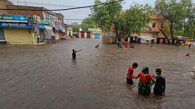 Locals wade through a flooded area after heavy monsoon rains, in Fatehpur (PTI)
