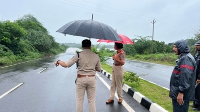 Police personnel cover their heads with umbrellas as they inspect the closed roads. (ANI Photo) Police personnel cover their heads with umbrellas as they inspect the closed roads. (ANI Photo)