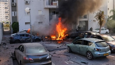 A member of the Israeli security forces stands near burning cars following a rocket attack from the Gaza Strip in Ashkelon, southern Israel, on October 7, 2023. (AFP) A member of the Israeli security forces stands near burning cars following a rocket attack from the Gaza Strip in Ashkelon, southern Israel, on October 7, 2023. (AFP)