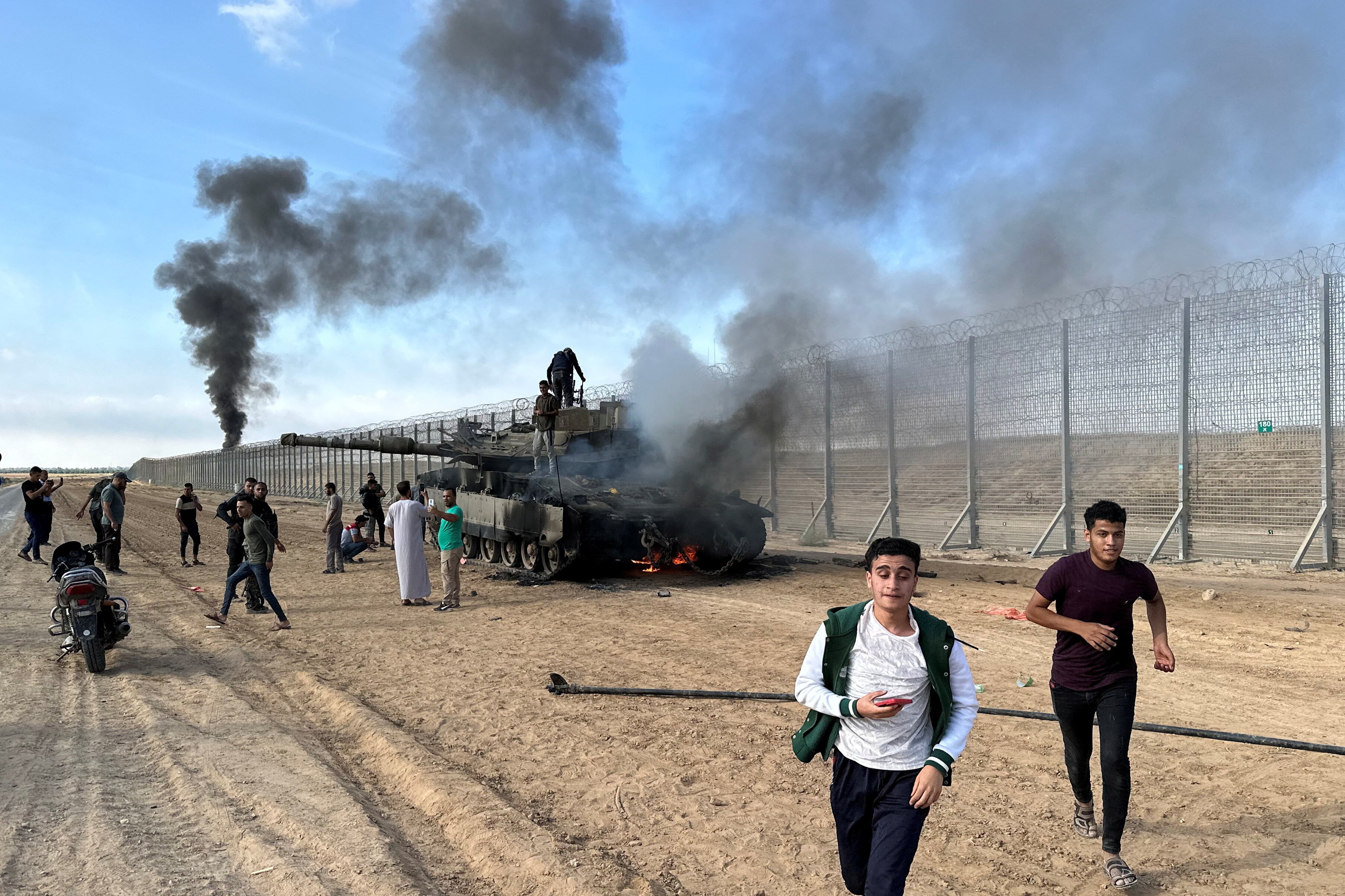 Palestinians react as an Israeli military vehicle burns after it was hit by Palestinian gunmen who infiltrated areas of southern Israel, at the Israeli side of Israel-Gaza border, October 7, 2023. REUTERS/Mohammed Fayq Abu Mostafa       NO RESALES. NO ARCHIVES. (REUTERS)