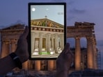 A man holds up a tablet showing a digitally overlayed virtual reconstruction of the ancient Parthenon temple, at the Acropolis Hill in Athens, Greece. A man holds up a tablet showing a digitally overlayed virtual reconstruction of the ancient Parthenon temple, at the Acropolis Hill in Athens, Greece.