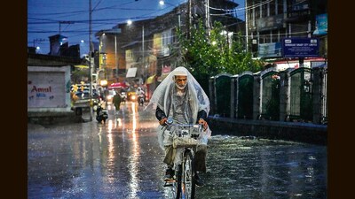 A man rides a bicycle while shielding from rain using plastic sheet in Srinagar on Monday. (AP) A man rides a bicycle while shielding from rain using plastic sheet in Srinagar on Monday. (AP)