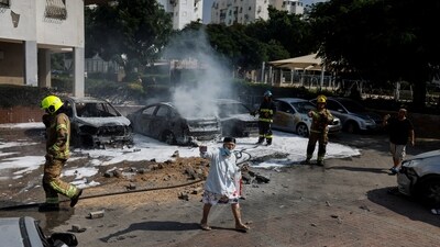Israeli firefighters work to put out vehicles on fire after a rocket, launched from the Gaza Strip, landed in Ashkelon, southern Israel (Reuters)