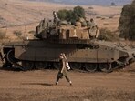 A female Israeli soldier walks in front of a stationed tank near the border with Israel in Lebanon on October 14. A female Israeli soldier walks in front of a stationed tank near the border with Israel in Lebanon on October 14.