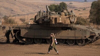 A female Israeli soldier walks in front of a stationed tank near the border with Israel in Lebanon on October 14. (AP)