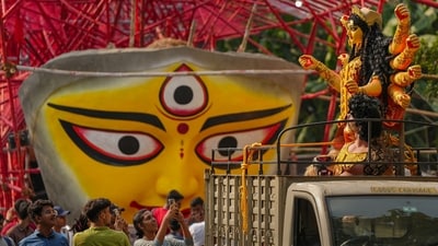 Clay idol of goddess Durga being transported, passing besides a community puja pandal where a big face of Devi Durga also being installed, for the Durga Puja festival in Kolkata. (PTI) Clay idol of goddess Durga being transported, passing besides a community puja pandal where a big face of Devi Durga also being installed, for the Durga Puja festival in Kolkata. (PTI)