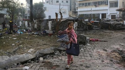 A girl carries blankets as she walks past the site of a deadly explosion at al-Ahli hospital in Gaza City (AP)