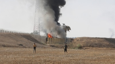 Israel-Hamas War: Palestinians stand by a burning Israeli military watch tower in the Gaza Strip. (AP) Israel-Hamas War: Palestinians stand by a burning Israeli military watch tower in the Gaza Strip. (AP)