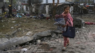A girl carries blankets as she walks past the site of a deadly explosion at al-Ahli hospital in Gaza City (AP) A girl carries blankets as she walks past the site of a deadly explosion at al-Ahli hospital in Gaza City (AP)