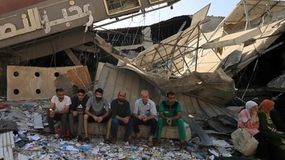 Israel-Hamas War: People sit in front of a bakery that was partially destroyed in an Israeli strike, in the Nuseirat refugee camp in the central Gaza Strip. (AFP)