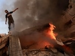 A Palestinian man gestures as he stands on the rubble of a collapsed building as a fire burns following a strike by the Israeli military on Khan Yunis in the southern Gaza Strip. (AFP)