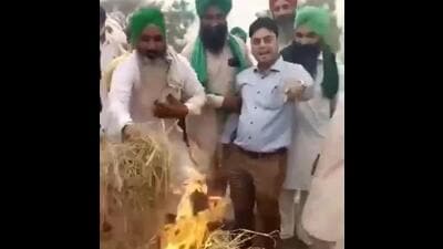 A video grab of farmers holding Punjab PWD sub divisional engineer Hardeep Sagar by the arm and forcing him to torch the paddy residue at Mehma Sarja village in Bathinda district on Friday. (Sourced) A video grab of farmers holding Punjab PWD sub divisional engineer Hardeep Sagar by the arm and forcing him to torch the paddy residue at Mehma Sarja village in Bathinda district on Friday. (Sourced)