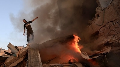 A Palestinian man gestures as he stands on the rubble of a collapsed building as a fire burns following a strike by the Israeli military on Khan Yunis in the southern Gaza Strip. (AFP)