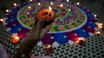 A girl holds an earthen lamp beside a rangoli, a hand decorated pattern on the floor, as part on Dhanteras celebration in Ahmedabad, (AP) A girl holds an earthen lamp beside a rangoli, a hand decorated pattern on the floor, as part on Dhanteras celebration in Ahmedabad, (AP)