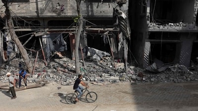 A Palestinian man rides his bicycle past destroyed buildings in Bureij, in the central of Gaza Strip, on November 14, 2023. (AFP) A Palestinian man rides his bicycle past destroyed buildings in Bureij, in the central of Gaza Strip, on November 14, 2023. (AFP)