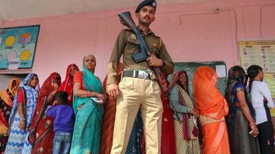 A police officer stands guard as women voters wait in queue to cast their votes at a polling booth during Madhya Pradesh Assembly elections, on the outskirts of Bhopal. (PTI)