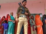 A police officer stands guard as women voters wait in queue to cast their votes at a polling booth