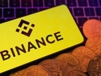 Smartphone with displayed Binance logo and representation of cryptocurrencies are placed on a keyboard in this illustration