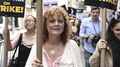 Susan Sarandon pick up a sign for the strike. Outside the Warner Bros. studios in Burbank, California, throngs of protesters chanted: “Fists up, curtains down, LA is a union town.” Food trucks flanking organizers' tents served churros, boba tea and cold lemonade to protesters baking in the midday heat that reached 98 degrees Fahrenheit (36.7 Celsius). Susan Sarandon pick up a sign for the strike. Outside the Warner Bros. studios in Burbank, California, throngs of protesters chanted: “Fists up, curtains down, LA is a union town.” Food trucks flanking organizers' tents served churros, boba tea and cold lemonade to protesters baking in the midday heat that reached 98 degrees Fahrenheit (36.7 Celsius). 