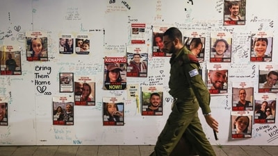A soldier walks in front of of images of Israeli hostages held in Gaza since the October 7 attack by Hamas militants in southern Israel, during a protest to ask for their release in Tel Aviv on November 22, 2023. (AFP)