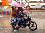 Commuter ride past during a rain, in Surat on Sunday.