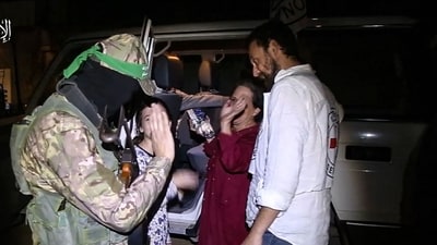 An image grab from a handout video released by the Hamas Media Office shows a Red Cross medic looking on as newly released Israeli hostages and a Hamas fighter wave goodbye before boarding a Red Cross vehicle, in the Gaza Strip early on November 26, 2023 (Photo by HAMAS MEDIA OFFICE / AFP) (AFP)
