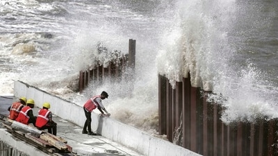 High tidal waves lash the shore as construction workers stand nearby. (PTI) High tidal waves lash the shore as construction workers stand nearby. (PTI)