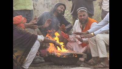 People sit near a bonfire to warm themselves on a cold winter morning in Gurugram on Sunday. (PTI)