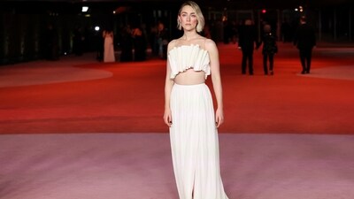 Saoirse Ronan looked ethereal on the red carpet in a Louis Vuitton strapless blouse featuring a structured swirl design. She styled it with a floor-length tulle skirt, glossy caramel-coloured lip shade, side-parted open locks, blushed cheeks, feathered brows, and a contoured face.&nbsp; (REUTERS)