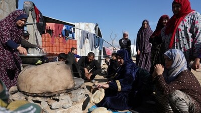 People wait while a woman prepares food, as displaced Palestinians, who fled their houses due to Israeli strike, shelter in a camp in Rafah, amid the ongoing conflict between Israel and Palestinian Islamist group Hamas, in the southern Gaza Strip on Dec 6. (Reuters)