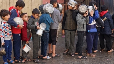 Palestinian children hold pots as they queue to receive food cooked by a charity kitchen, amid shortages in food supplies. (REUTERS)