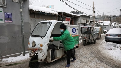 A delivery worker pushes a vehicle towed by a scooter at a hutong alley following snowfall in Beijing. (REUTERS)