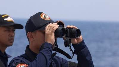 A Philippine Coast Guard personnel looks through a binocular while conducting a resupply mission for Filipino troops stationed at a grounded warship in the South China Sea. (Reuters)
