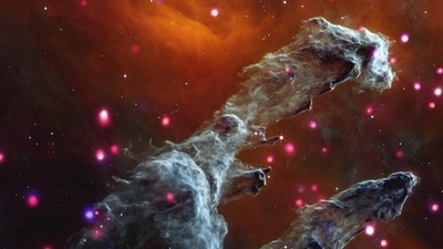 Columns of gray gas and dust emerge amid The Eagle Nebula, also called M16, and often referred to as the "Pillars of Creation" in a composite image taken by the James Webb Telescope and released by NASA on May 23, 2023. Backed by dark orange mist, the cloudy gray columns are surrounded by dozens of soft, glowing, pink and purple dots; massive stars emitting enormous amounts of X-rays.&nbsp; (NASA/ESA via REUTERS)