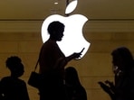 A women uses an iPhone mobile device as she passes a lighted Apple logo at the Apple store