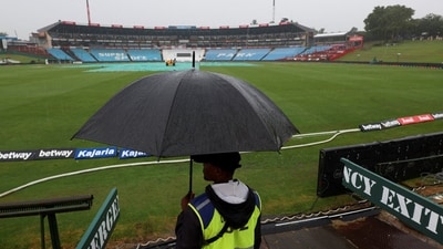 A security guard holds an umbrella, as the pitch and part of the ground is covered, during rain, a day before the first cricket test match between South Africa and India at SuperSport Park Cricket Stadium, in Centurion (REUTERS)