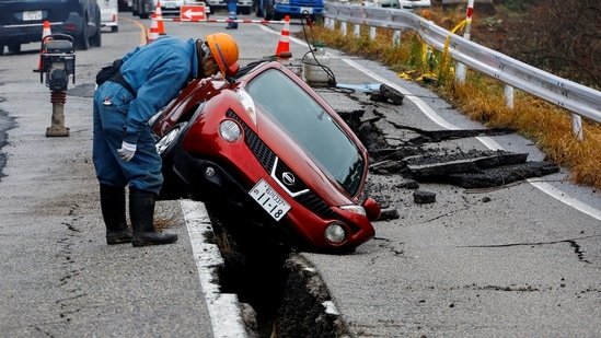 A worker looks at a car stuck on a broken road in the aftermath of an earthquake near Anamizu, Japan.(REUTERS)