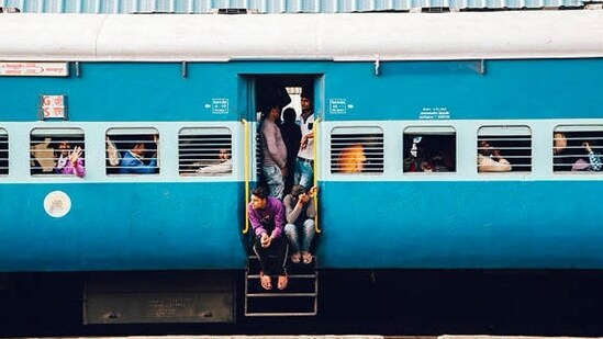 Passengers sitting next to the door of a moving train. (X/@RailMinIndia)