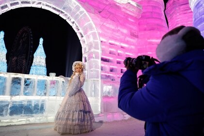 A woman dressed up in a costume gets clicked in front of  an ice sculpture of  a castle