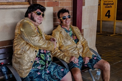 Two men dressed as Elvis sit on a bench as people board a train to travel to the annual Parkes Elvis Festival | Photo: AFP